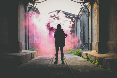 Full length of silhouette person standing by abandoned building with pink smoke in background