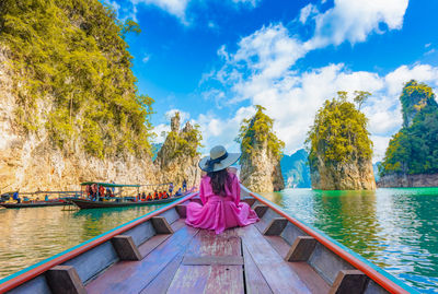 Rear view of woman sitting on boat in lake against sky