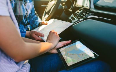 Midsection of couple using digital tablet while sitting in car