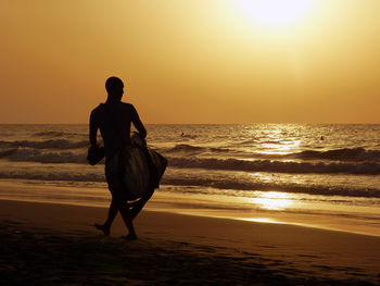 Full length of silhouette man walking at beach against orange sky