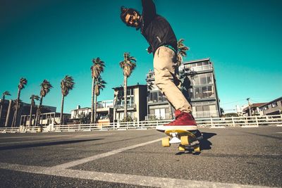 Man skateboarding on street in city against clear sky