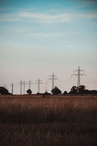 Electricity pylons on field against sky