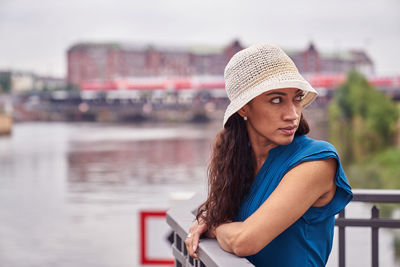 Woman wearing hat by river in city