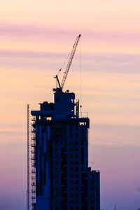 Silhouette crane at construction site against sky during sunset