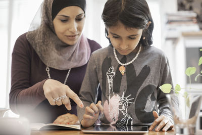 Mother assisting daughter using digital tablet at home