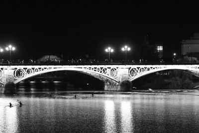 Illuminated bridge over river against sky at night