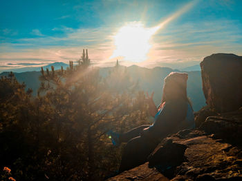 Man sitting on rock against sky during sunset