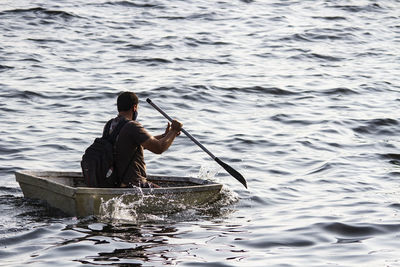 Rear view of man wearing mask sitting on boat in lake