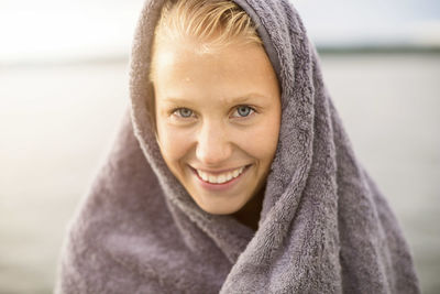 Portrait of smiling woman wrapped in towel at lakeshore