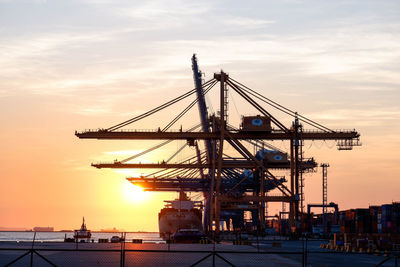 Cranes at commercial dock against sky during sunset