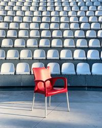 Empty red chair against white bleachers at stadium