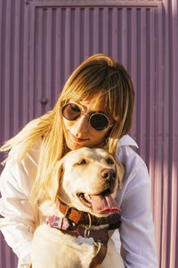 Woman wearing sunglasses embracing pet dog on sunny day