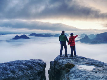 Lovers mirroring in water eye at mountain summit above thick mist. climbing for mazing aerial view