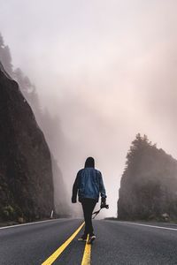 Rear view of man walking on road against sky