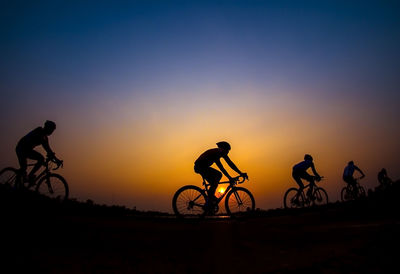 Silhouette friends riding bicycle against sky during sunset