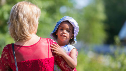 Mother carrying daughter at park on sunny day