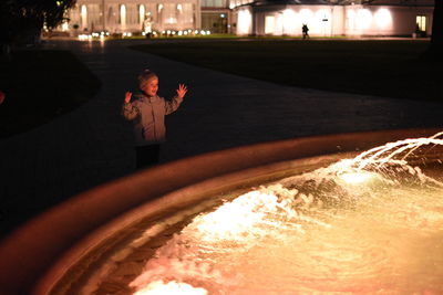 Rear view of boy standing by illuminated light at night