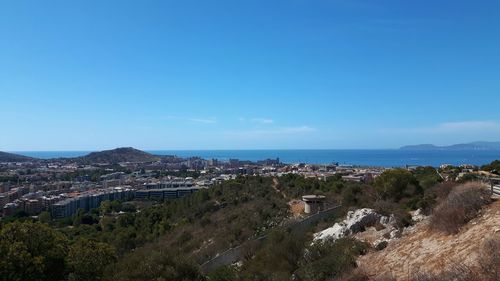 Aerial view of townscape by sea against blue sky