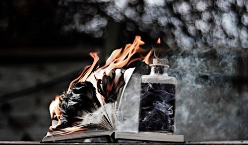 Smoke emitting from burning book and oil lamp on table