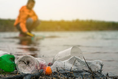 Close-up of plastic bottles at lakeshore with boy crouching in background