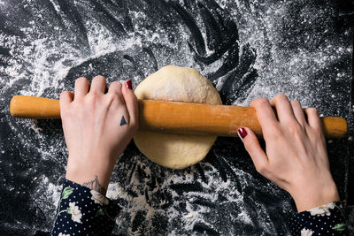 Cropped hands of woman rolling dough in kitchen