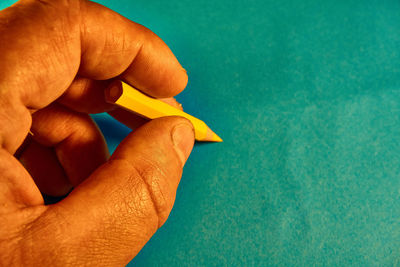 Close-up of hand holding leaf against blue background