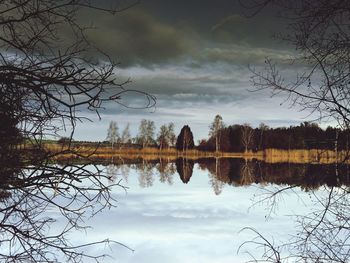 Reflection of bare trees in lake against sky