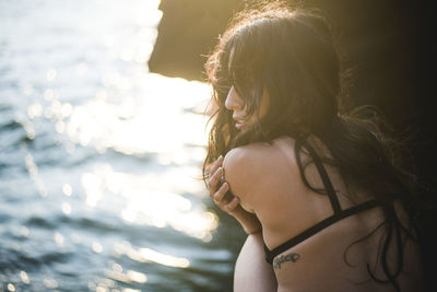 Young latina woman sitting by the ocean at golden hour in summertime