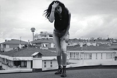 Full length portrait of young woman bending on roof against sky
