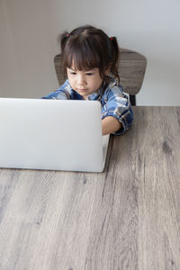 Cute girl using mobile phone while sitting on table