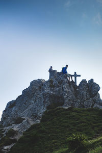 Low angle view of boys on rock against clear sky