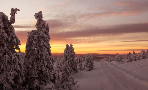 Snow covered landscape against sky during sunset