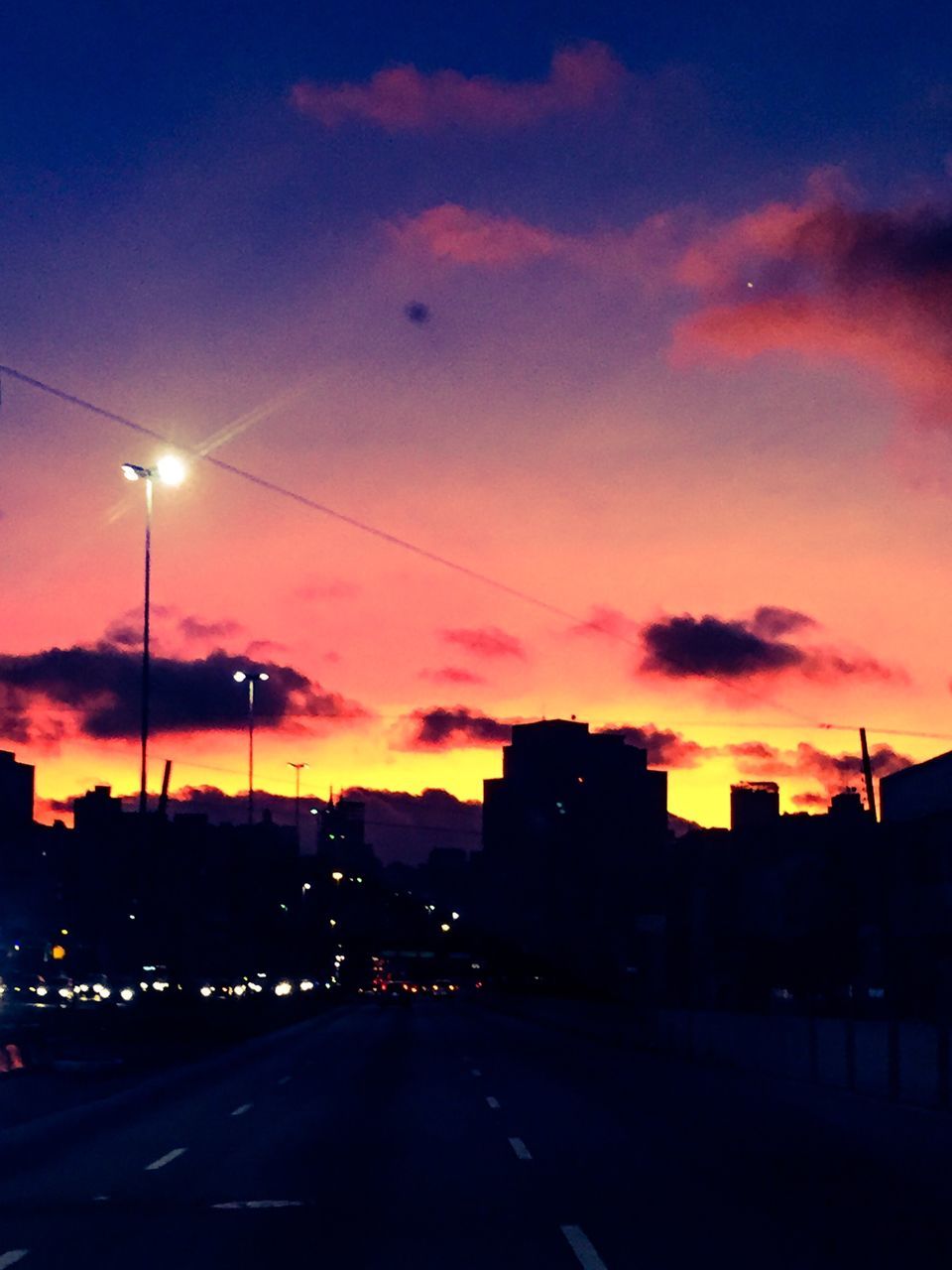 sunset, street light, sky, illuminated, silhouette, road, the way forward, transportation, building exterior, dusk, orange color, cloud - sky, street, lighting equipment, architecture, built structure, outdoors, diminishing perspective, road marking, cloud