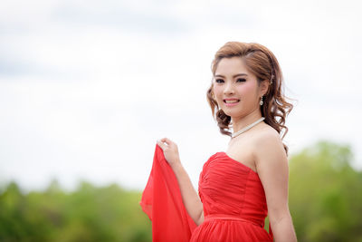 Portrait of smiling young woman standing against sky