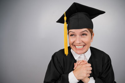 Portrait of man wearing graduation gown against white background