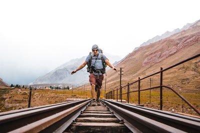 Male hiker walking on railroad track against mountains