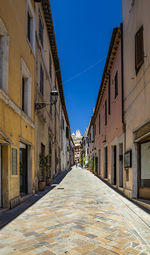 Empty alley amidst buildings against blue sky