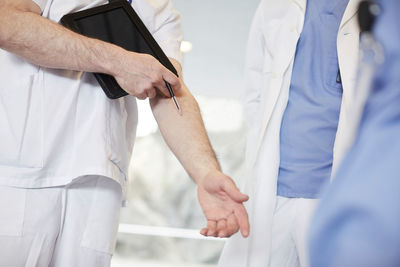 Midsection of male nurse gesturing while standing with coworkers at hospital