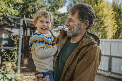 Father laughing while carrying son standing in back yard on sunny day