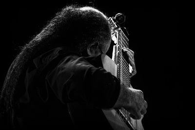 Side view of man playing guitar while sitting against black background