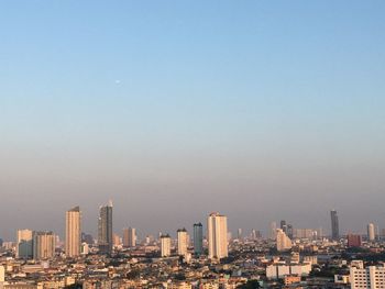 Modern buildings in city against clear sky with airplane