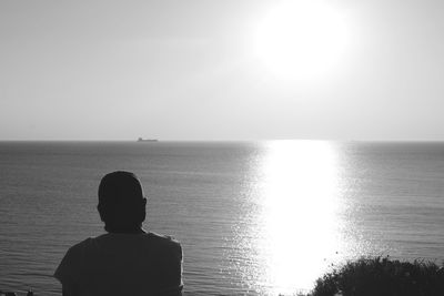 Rear view of silhouette man standing in sea against sunset sky