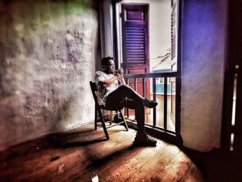 Side view of woman sitting by window at home