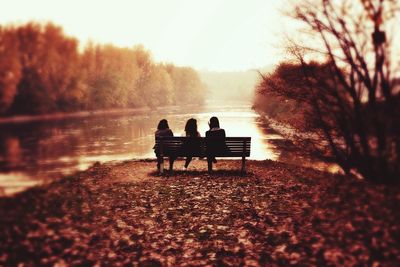 Rear view of friends sitting on bench at lakeshore