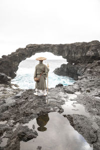 Mature monk with stick standing in front of rock arch