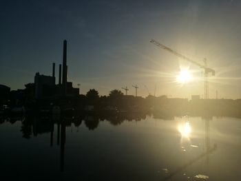 Silhouette buildings by lake against sky during sunset
