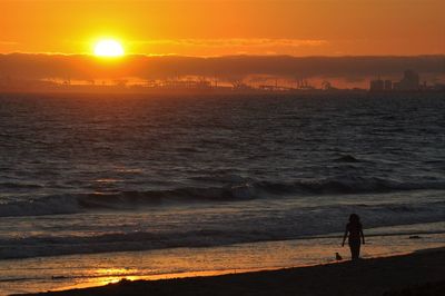 Silhouette people standing on shore against sky during sunset