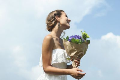 Young woman holding bouquet against sky