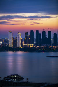 Illuminated buildings in city against sky during sunset