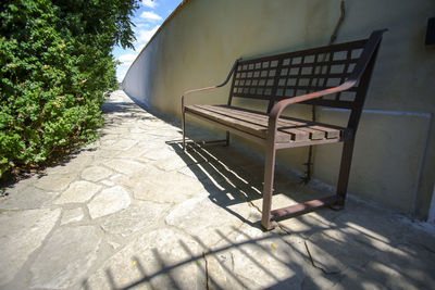 High angle view of empty bench on footpath during sunny day